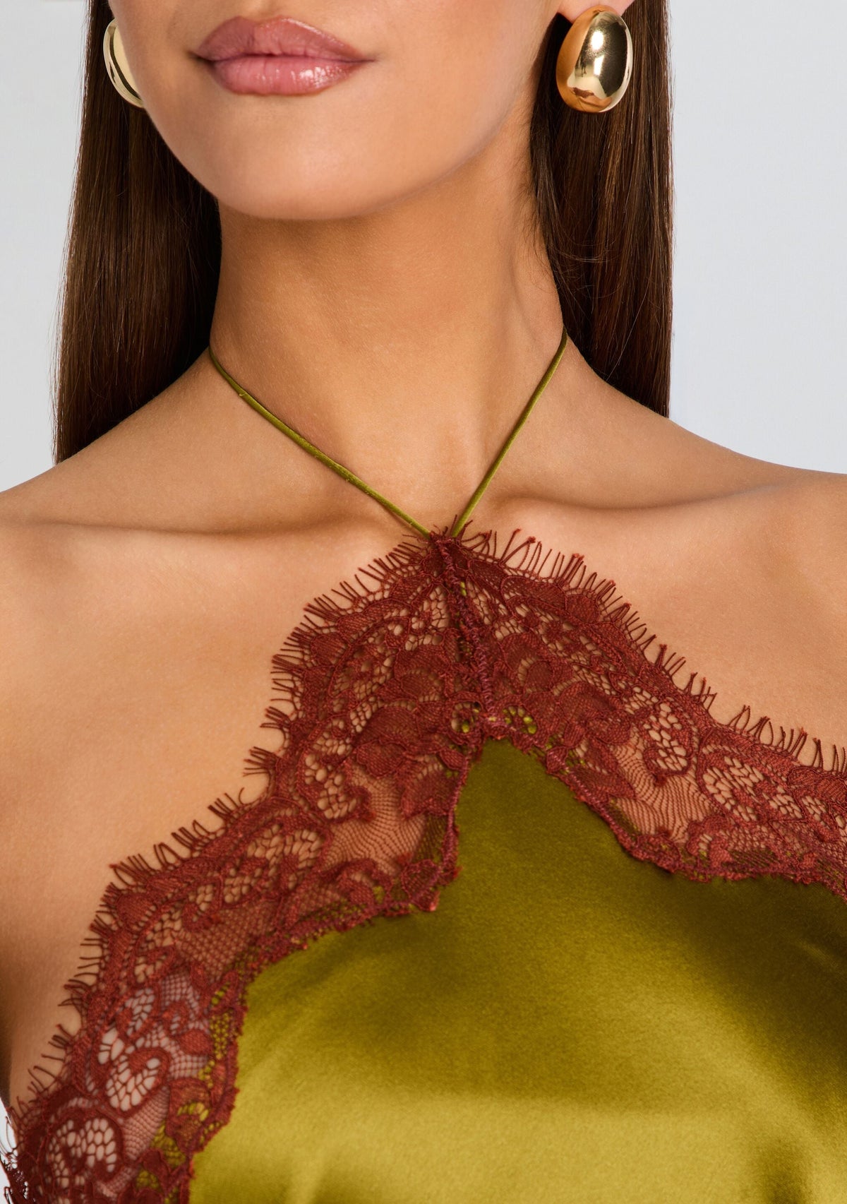 Close-up of a person wearing a green dress with lace detailing and gold earrings.